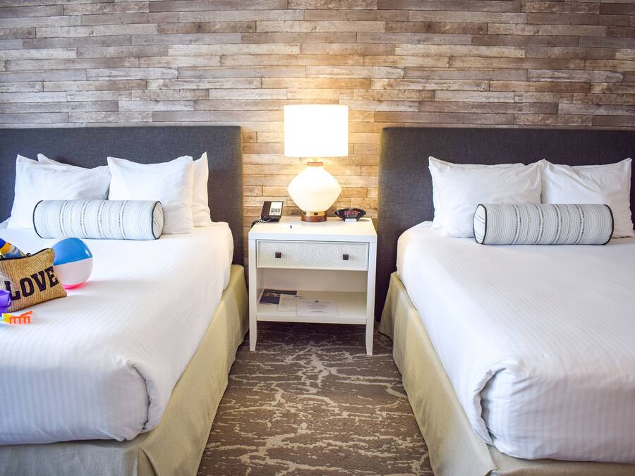 A hotel room with two beds, a nightstand with a lamp, and a brick wall.