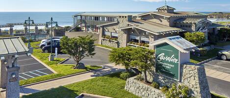 Um hotel à beira-mar com uma placa grande virada para o oceano, área de estacionamento e vista para o mar.