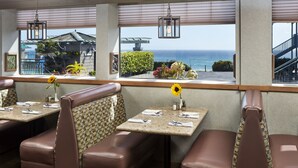 Un restaurante con asientos tipo cabina, vistas al océano y un patio con plantas y barandilla.