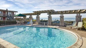 Piscina con sillas de descanso y una pérgola, con vista a un cuerpo de agua.