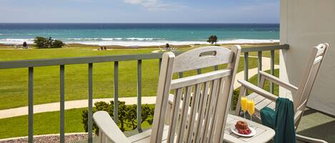 A balcony with a view of the ocean, a table with a plate of food and drinks, and two rocking chairs.