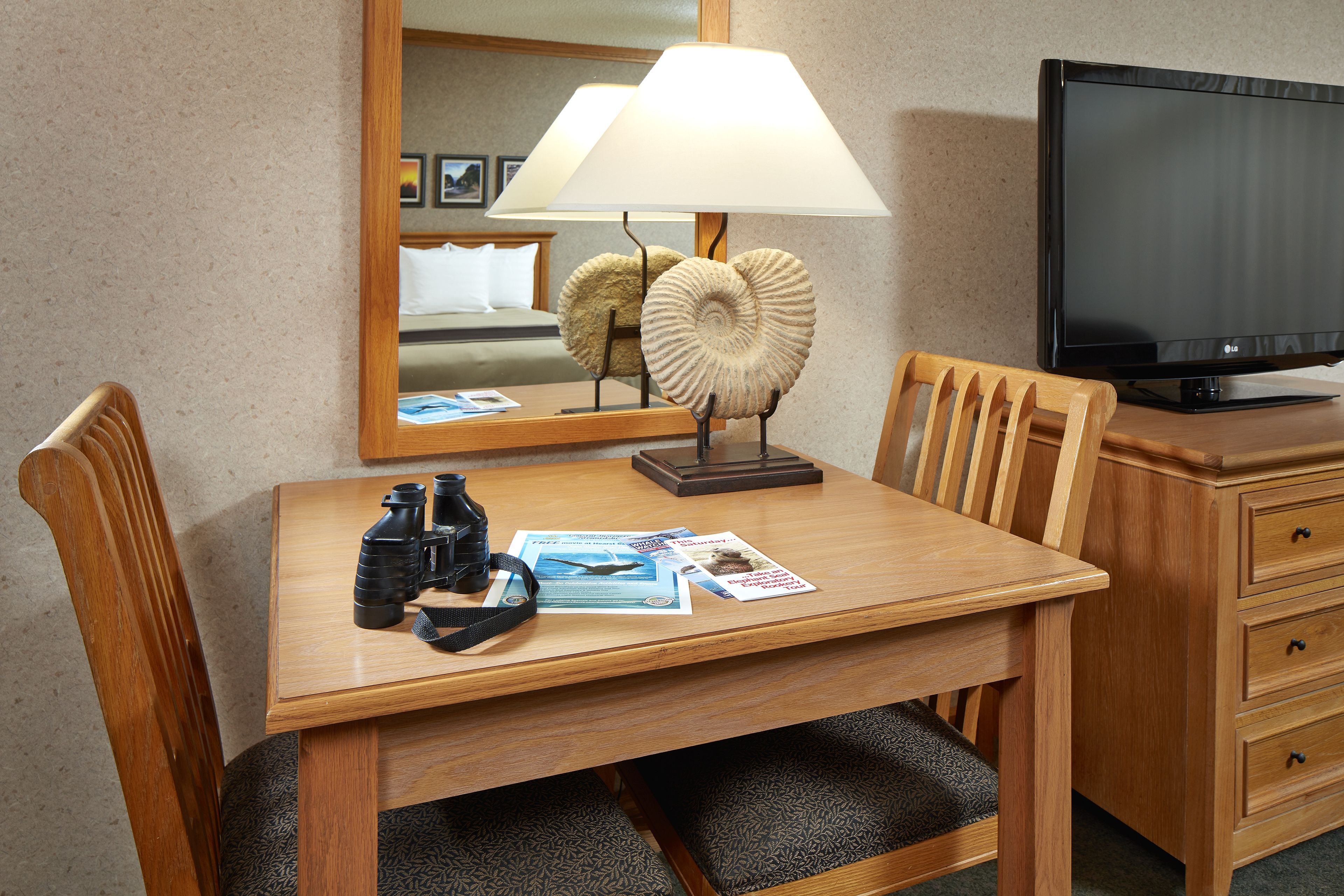 A hotel room with a wooden desk, a lamp, a television, and a mirror.