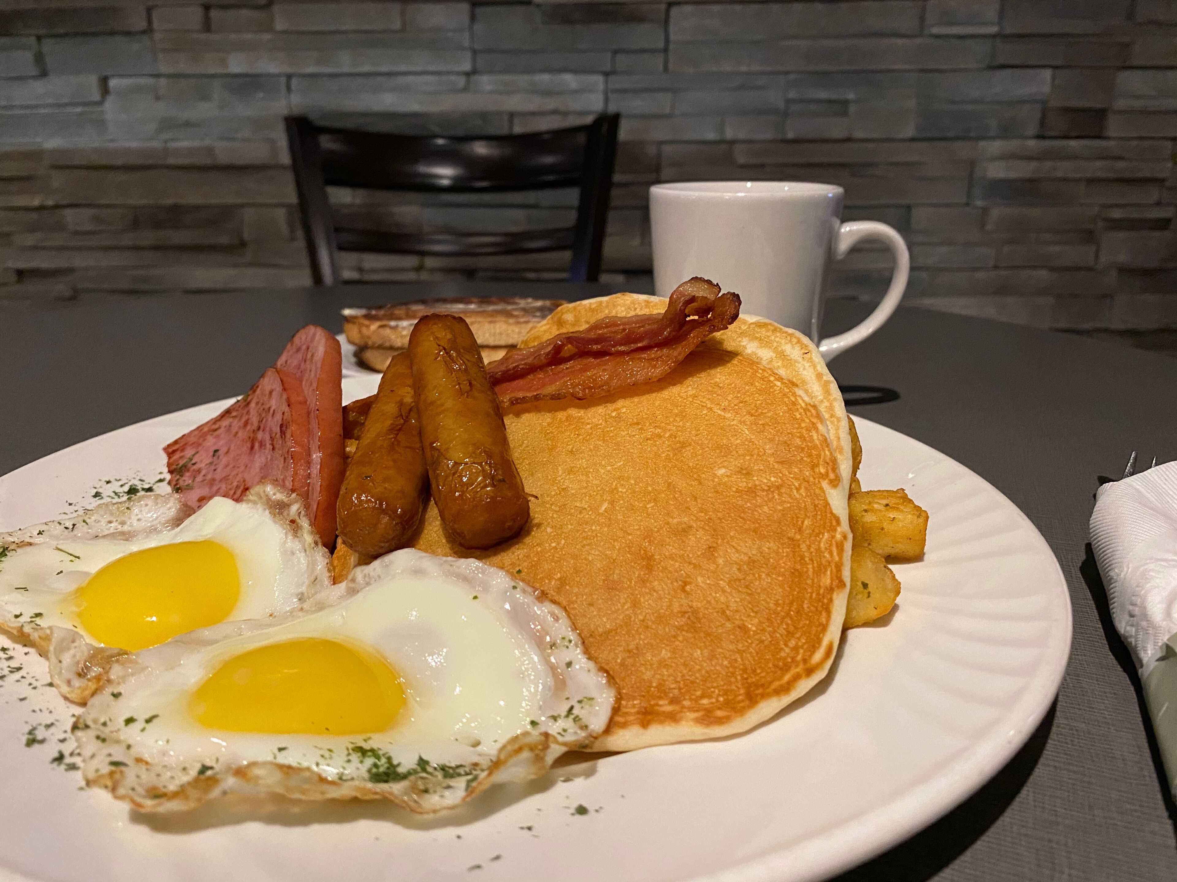 A breakfast plate with eggs, bacon, sausages, and hash browns on a white plate.