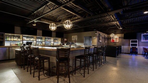 A bar area with a counter, bar stools, and shelves of bottles. - Travelodge by Wyndham Grande Prairie (Grande Prairie)
