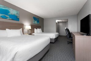 A hotel room with two beds, a desk with a television, a chair, a lamp, and artwork on the walls.