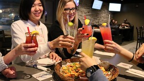A group of people toasting with drinks at a restaurant with a stone wall and TVs in the background. - Travelodge by Wyndham Grande Prairie (Grande Prairie)