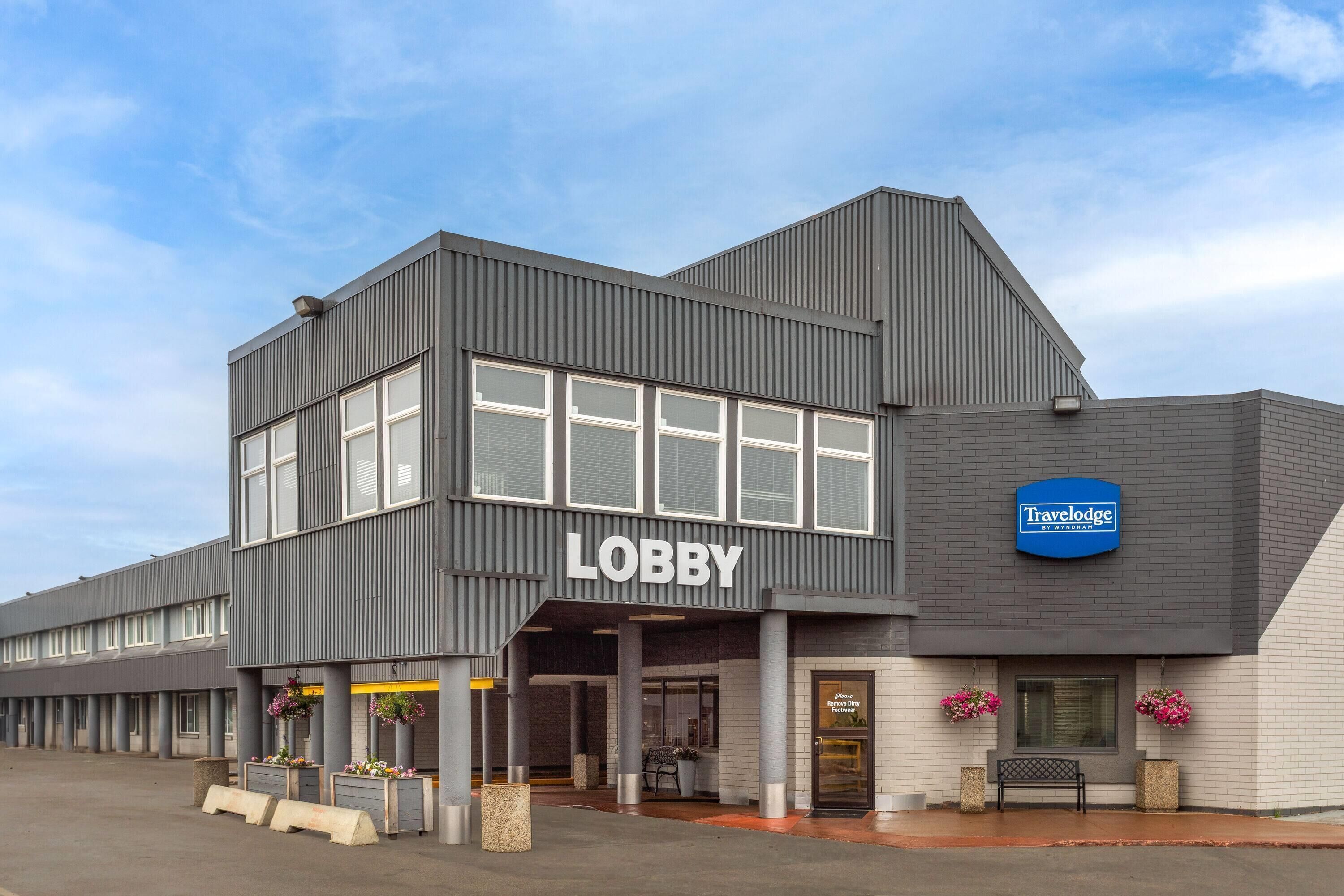 Een modern gebouw met een bord waarop 'Lobby' staat, een bord met 'Travelodge by Wyndham' en een bord met de tekst 'Schoenen schoonmaken, alstublieft'.