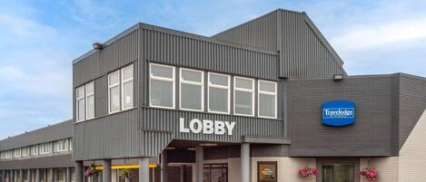 Een modern gebouw met een bord waarop 'Lobby' staat, een bord met 'Travelodge by Wyndham' en een bord met de tekst 'Schoenen schoonmaken, alstublieft'.