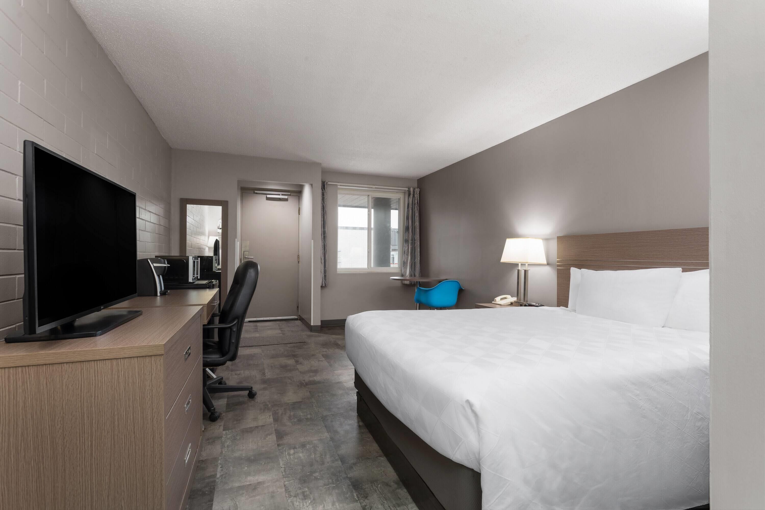 Una habitación de hotel con una cama, un escritorio con televisión, una silla, una lámpara y una ventana.