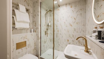 A bathroom with a glass-enclosed shower, a white sink with a gold faucet, and marble-patterned tiles.