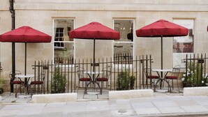 A building with outdoor seating, including tables and chairs, and red umbrellas.