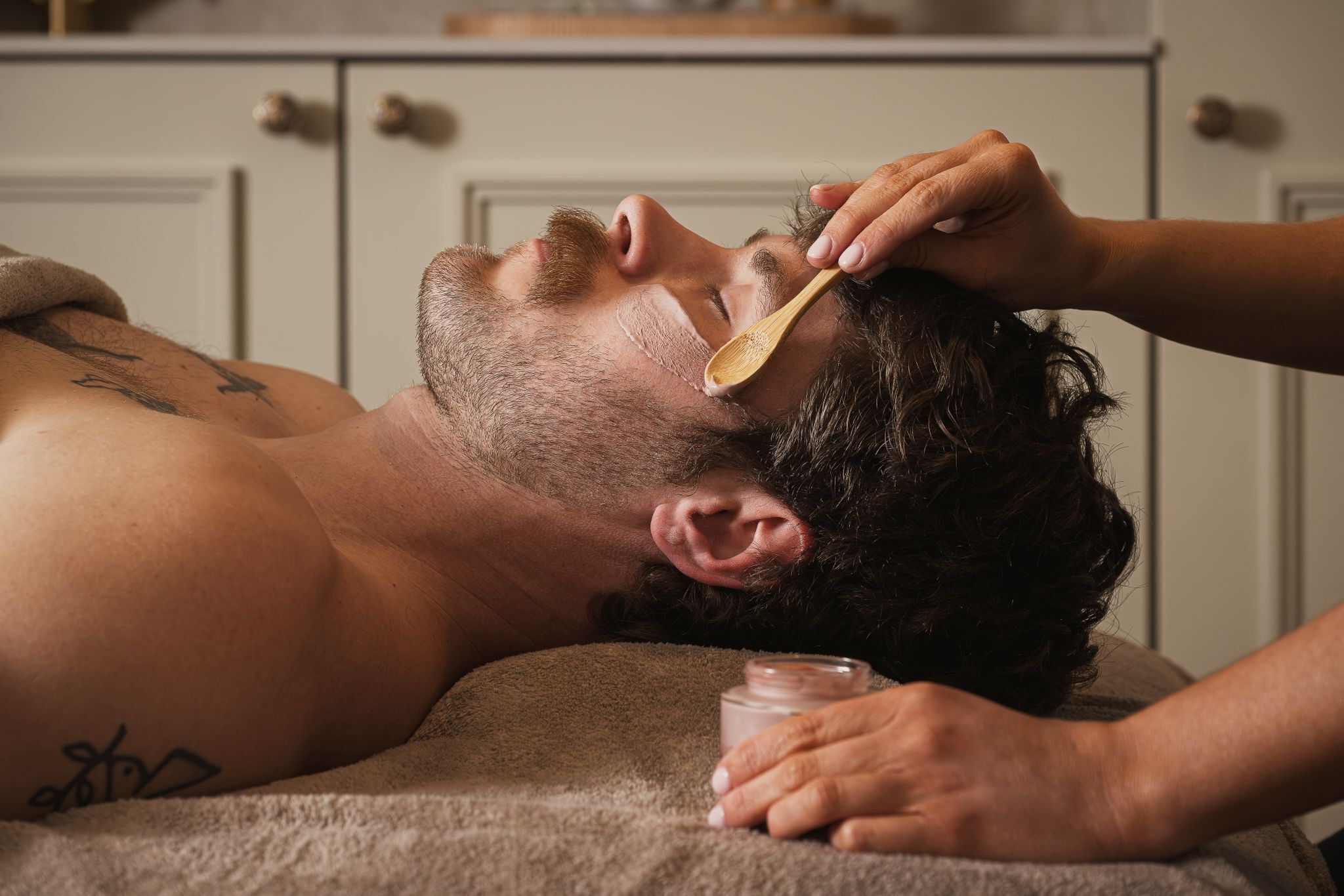 A person lying down with a towel, a wooden spoon, and a jar nearby.