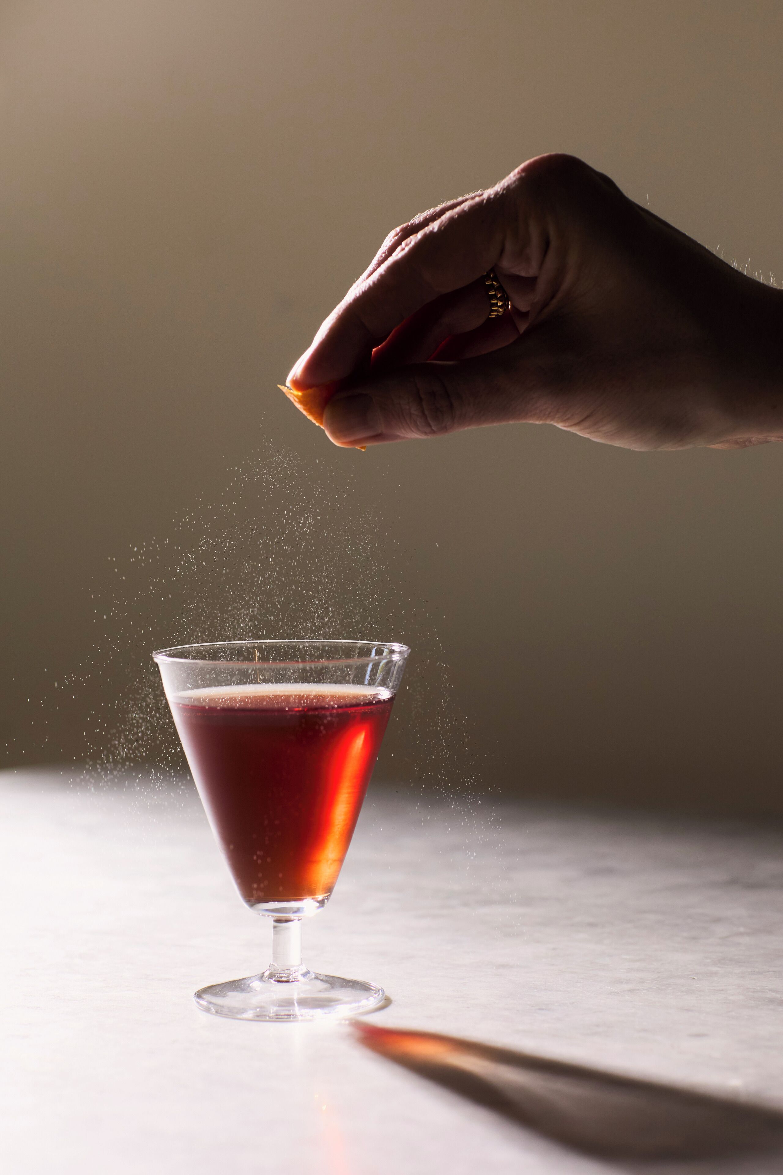 A hand sprinkling a powdery substance into a glass of red liquid.