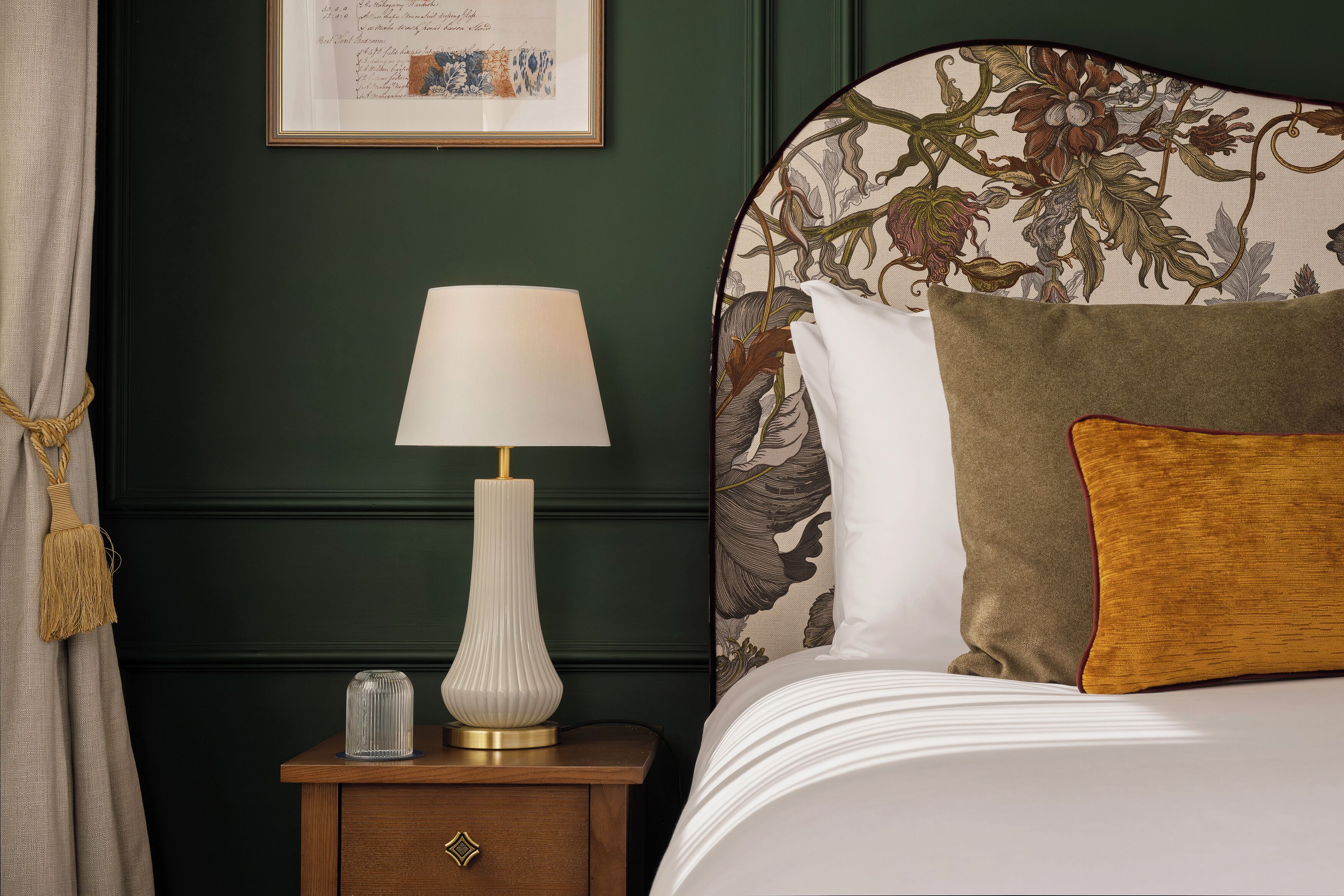 A neatly made bed with a floral headboard, a bedside lamp, and a framed picture on the wall.