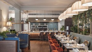 Un restaurante con una zona de bar, asientos con mesas dispuestas para comer y una barra.
