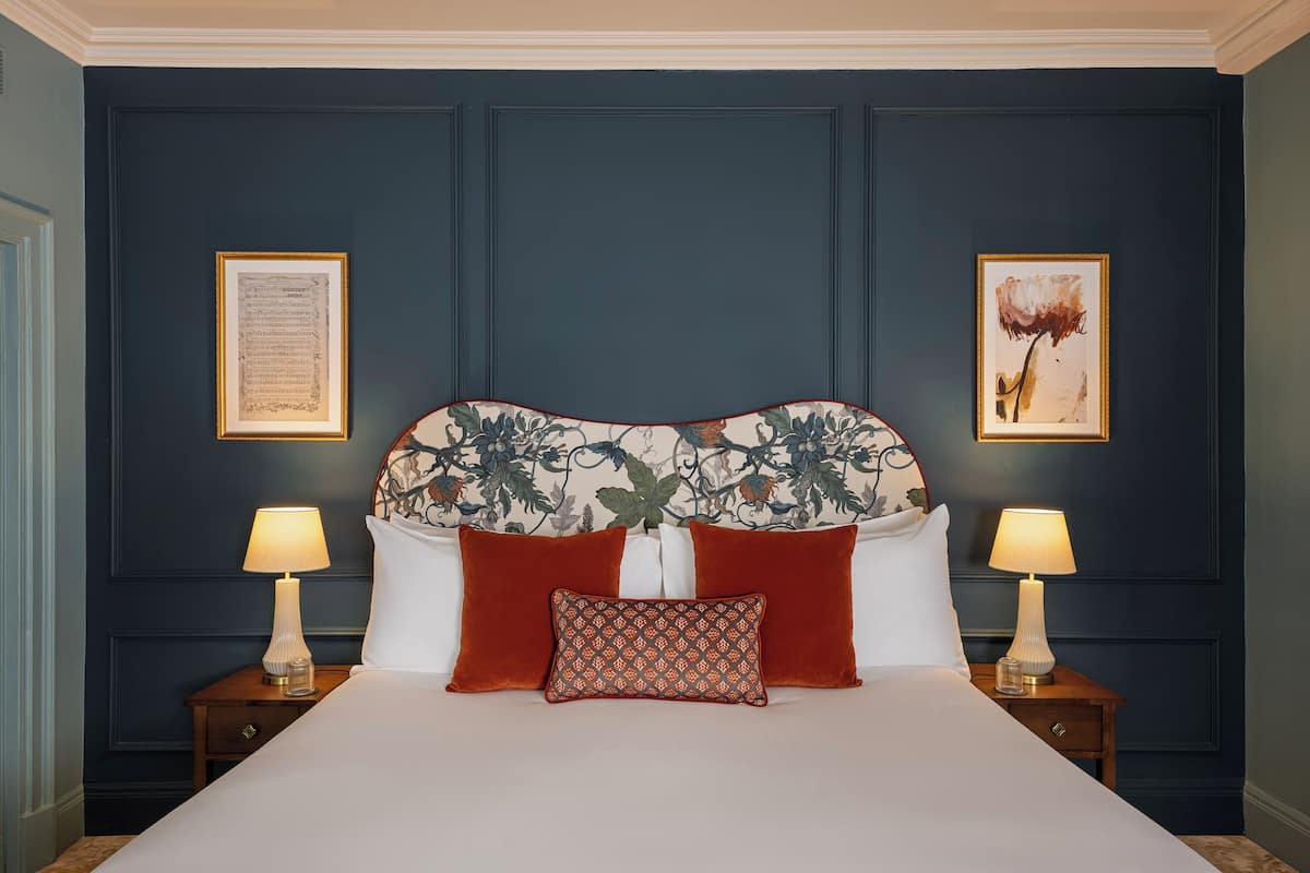 Ein Bett mit Blumenmuster am Kopfteil, zwei Nachttische mit Lampen und zwei gerahmte Bilder an der Wand.