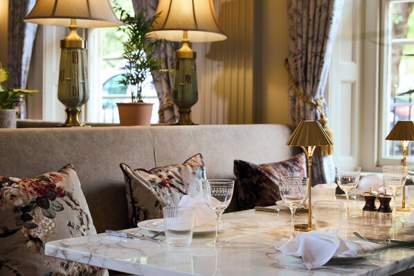 A dining area with a table set for two, featuring a marble top, clear glassware, and a gold lamp. - Francis Hotel Bath (Bath)