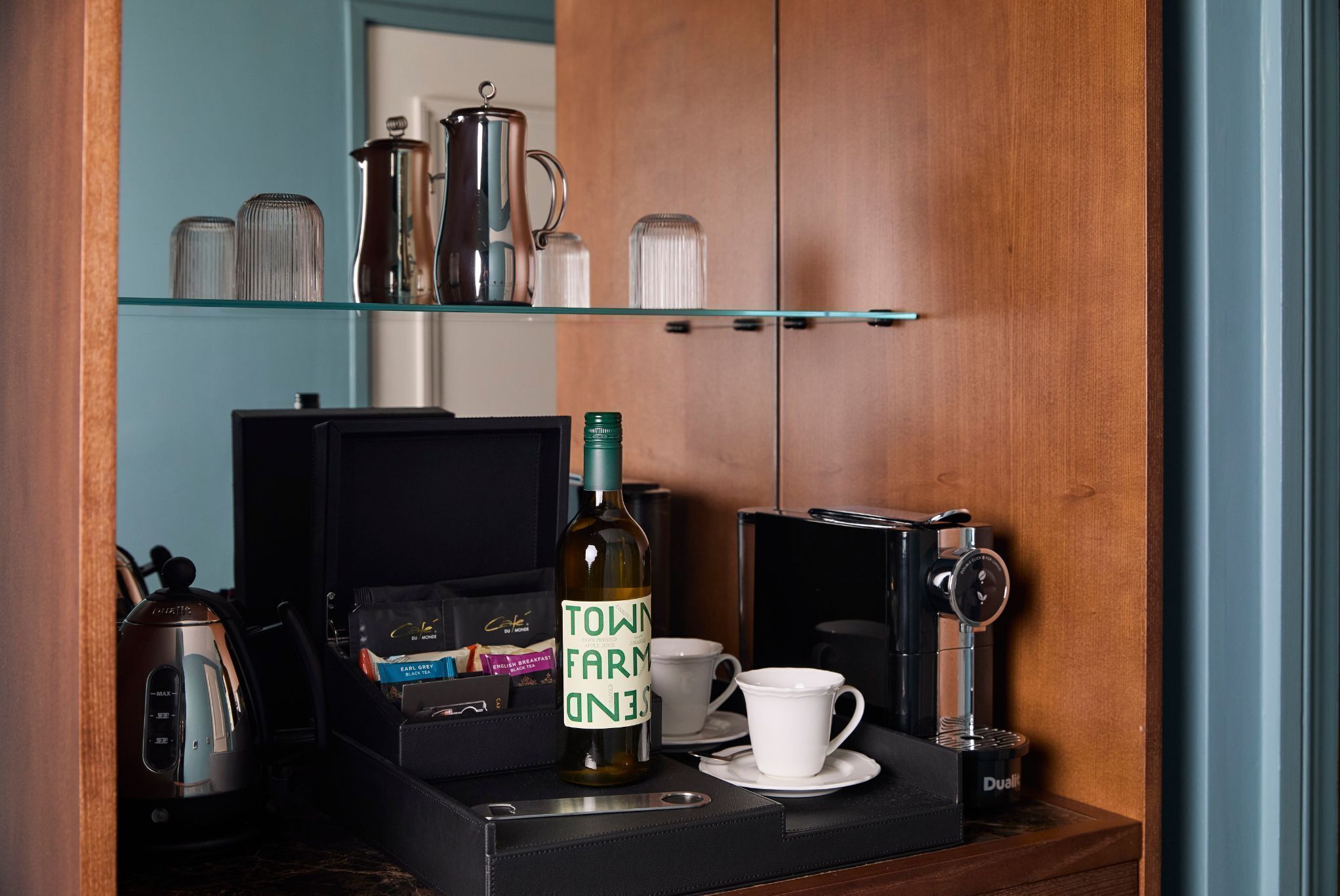 A coffee station with a coffee machine, a bottle of wine, and a cup on a tray.