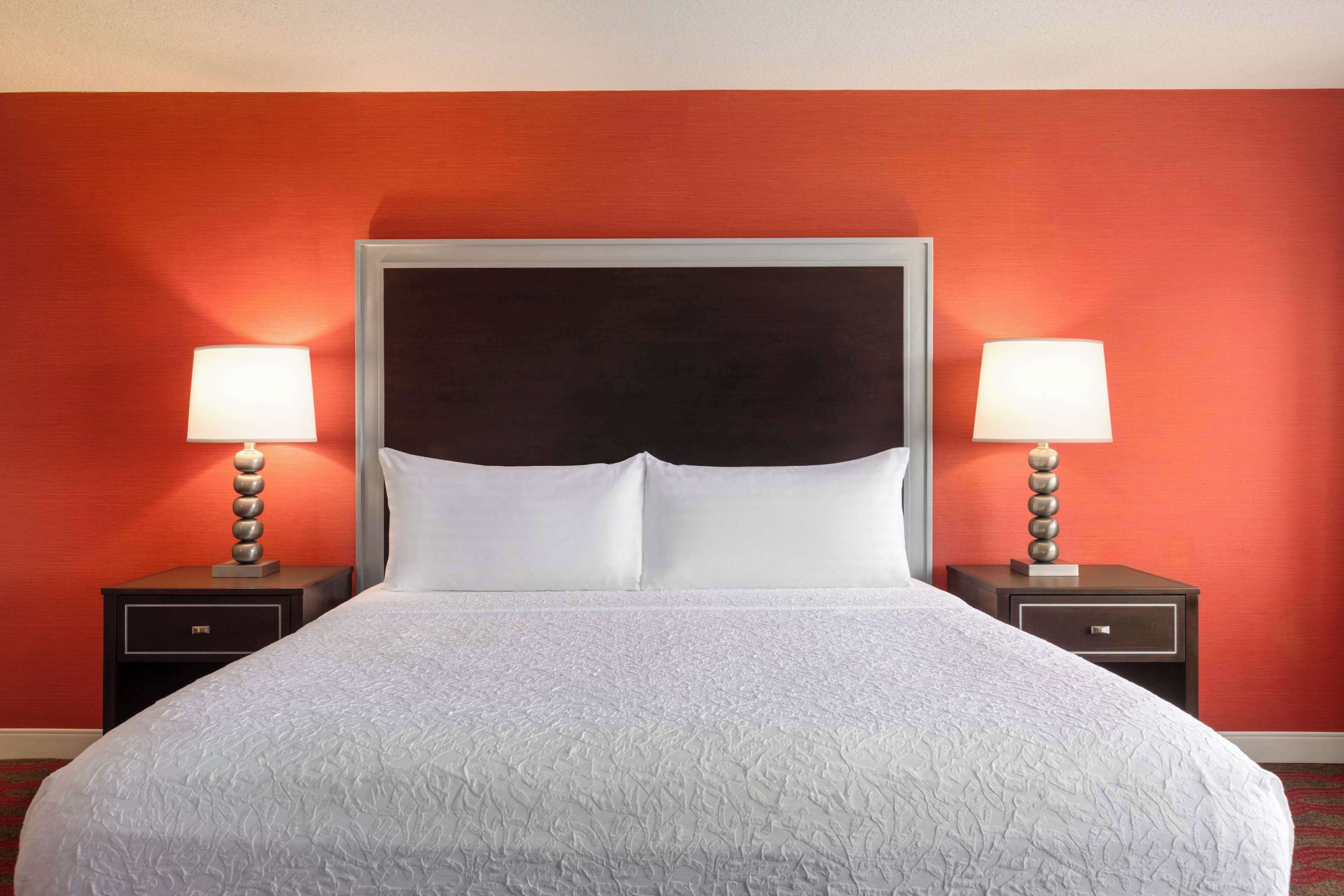 Una habitación de hotel con una cama grande, dos mesitas de noche con lámparas y una pared roja.