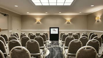 A conference room with rows of chairs, a podium, and wall-mounted lighting.