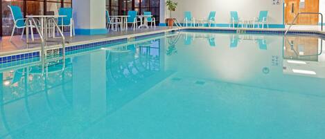 Una piscina interior con agua cristalina, rodeada de sillas y mesas de descanso.