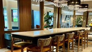 A long dining table with six chairs, surrounded by large windows and a chandelier. - DoubleTree by Hilton New York LaGuardia Airport (East Elmhurst)