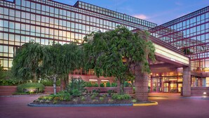 A modern hotel with a glass facade, outdoor seating area, and a well-maintained garden. - DoubleTree by Hilton New York LaGuardia Airport (East Elmhurst)