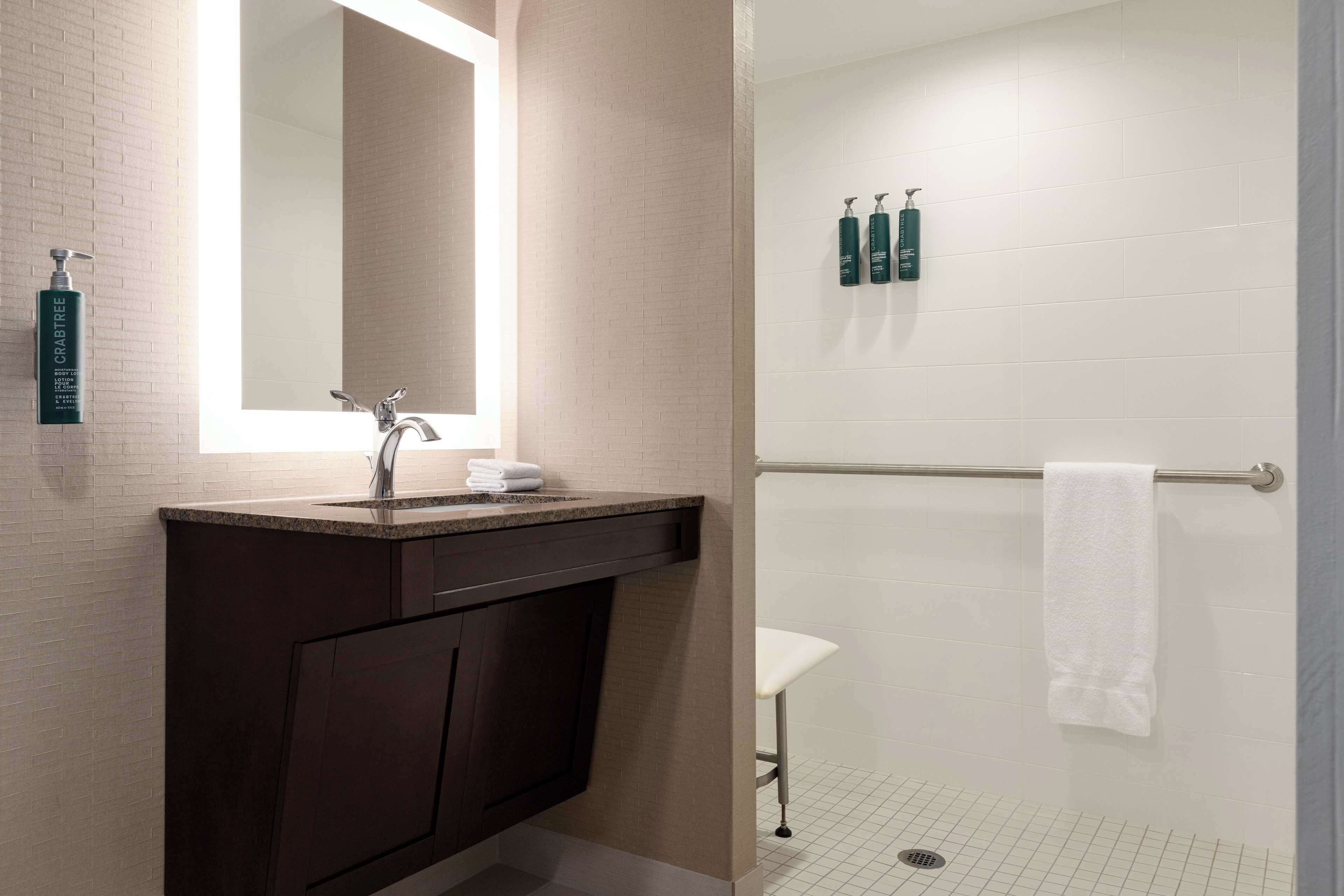 Un baño moderno con tocador oscuro, un espejo grande y zona de ducha con perchero.