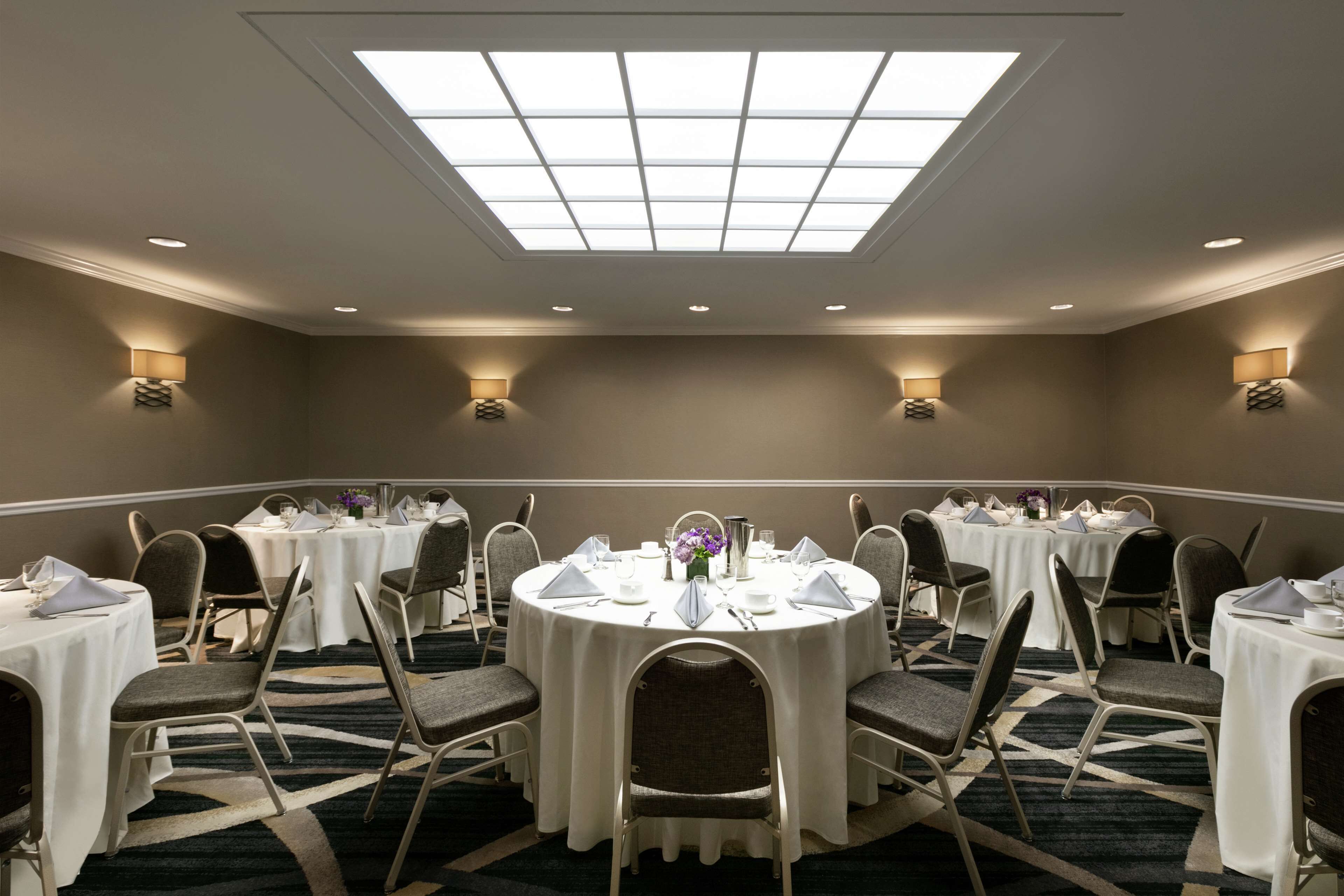 A conference room with multiple round tables, chairs, and ceiling lights.