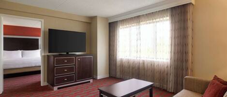 A hotel room with a bed, a TV, a sofa, a table, and a window with curtains.