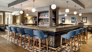 A bar area with a marble countertop, bar stools, hanging pendant lights, and a liquor display. - DoubleTree by Hilton New York LaGuardia Airport (East Elmhurst)