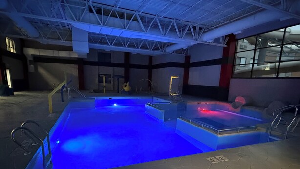 Une piscine intérieure dotée d’un élément décoratif aquatique illuminé de lumière bleue, d’un espace détente et d’une vue sur l’extérieur grâce à de grandes fenêtres.