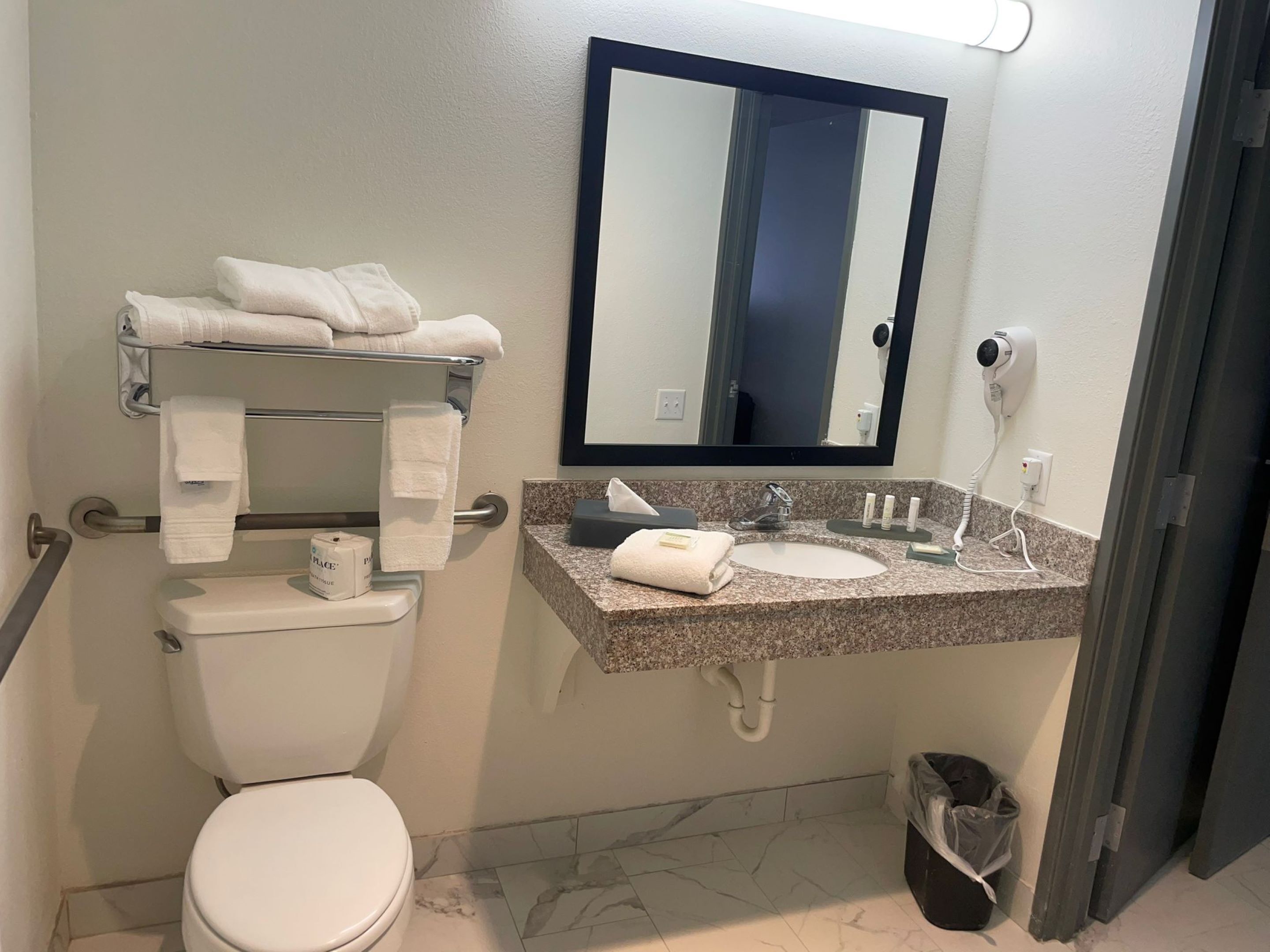 Un baño con inodoro, lavamanos con espejo y toallero con toallas.