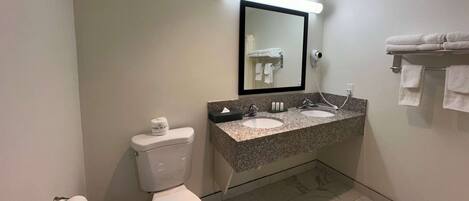 Un baño con inodoro, dos lavamanos, un espejo y un perchero para toallas.