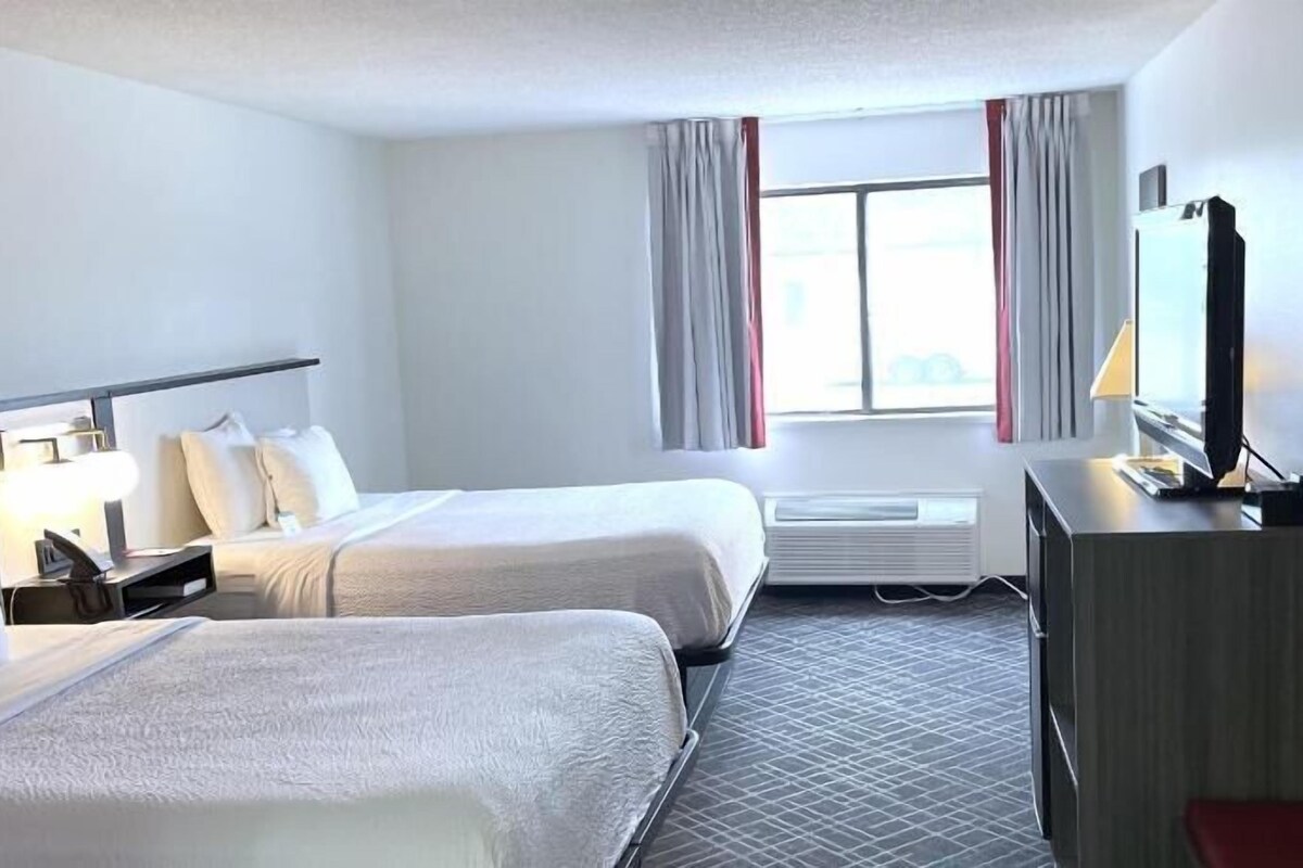 A hotel room with two beds, a desk, a television, and a window with curtains.
