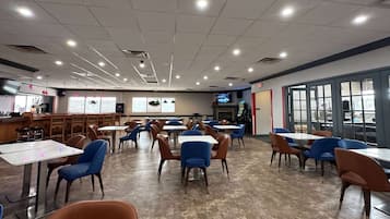 A spacious cafeteria with multiple tables and chairs, a counter area, and large windows.