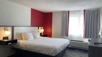 Une chambre d’hôtel avec un lit, des tables de chevet, un bureau et une fenêtre avec des rideaux.