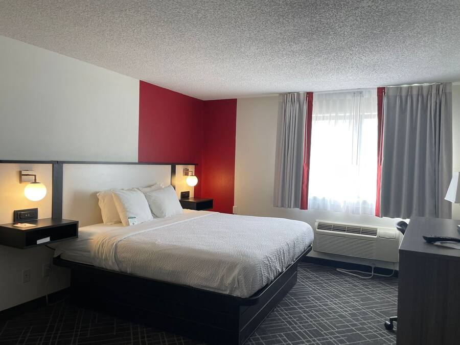 Une chambre d’hôtel avec un lit, des tables de chevet, un bureau et une fenêtre avec des rideaux.