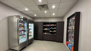 Une pièce propre et bien éclairée, équipée de deux distributeurs de boissons, de meubles de rangement en bois foncé et d’un présentoir mural où sont exposés divers articles.