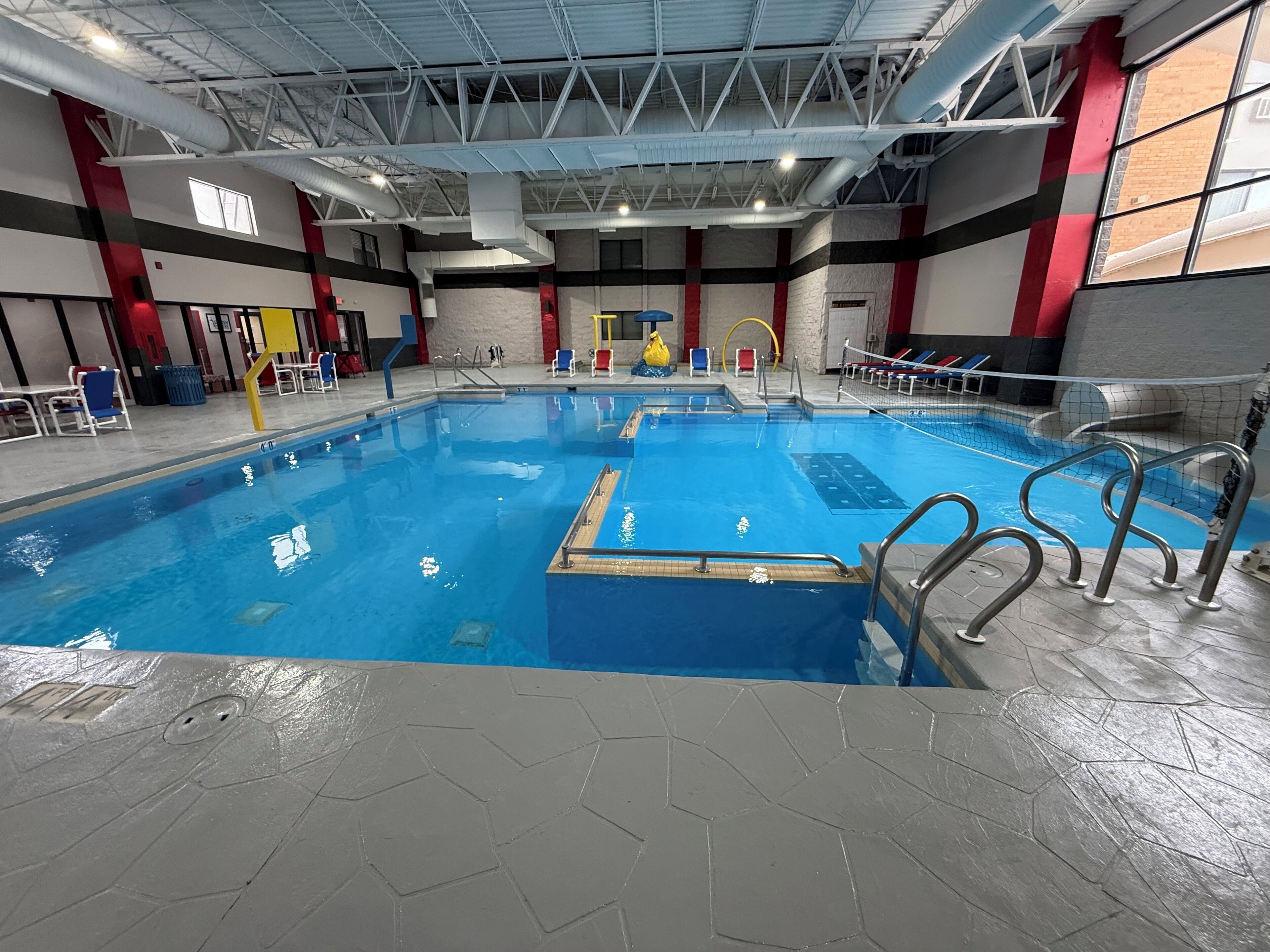 An indoor swimming pool with clear lanes, safety railings, and a tiled floor.