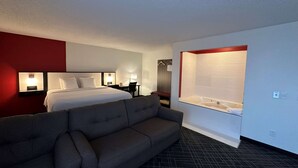 Une chambre d’hôtel avec un lit, un canapé, un bureau, une lampe et une baignoire.