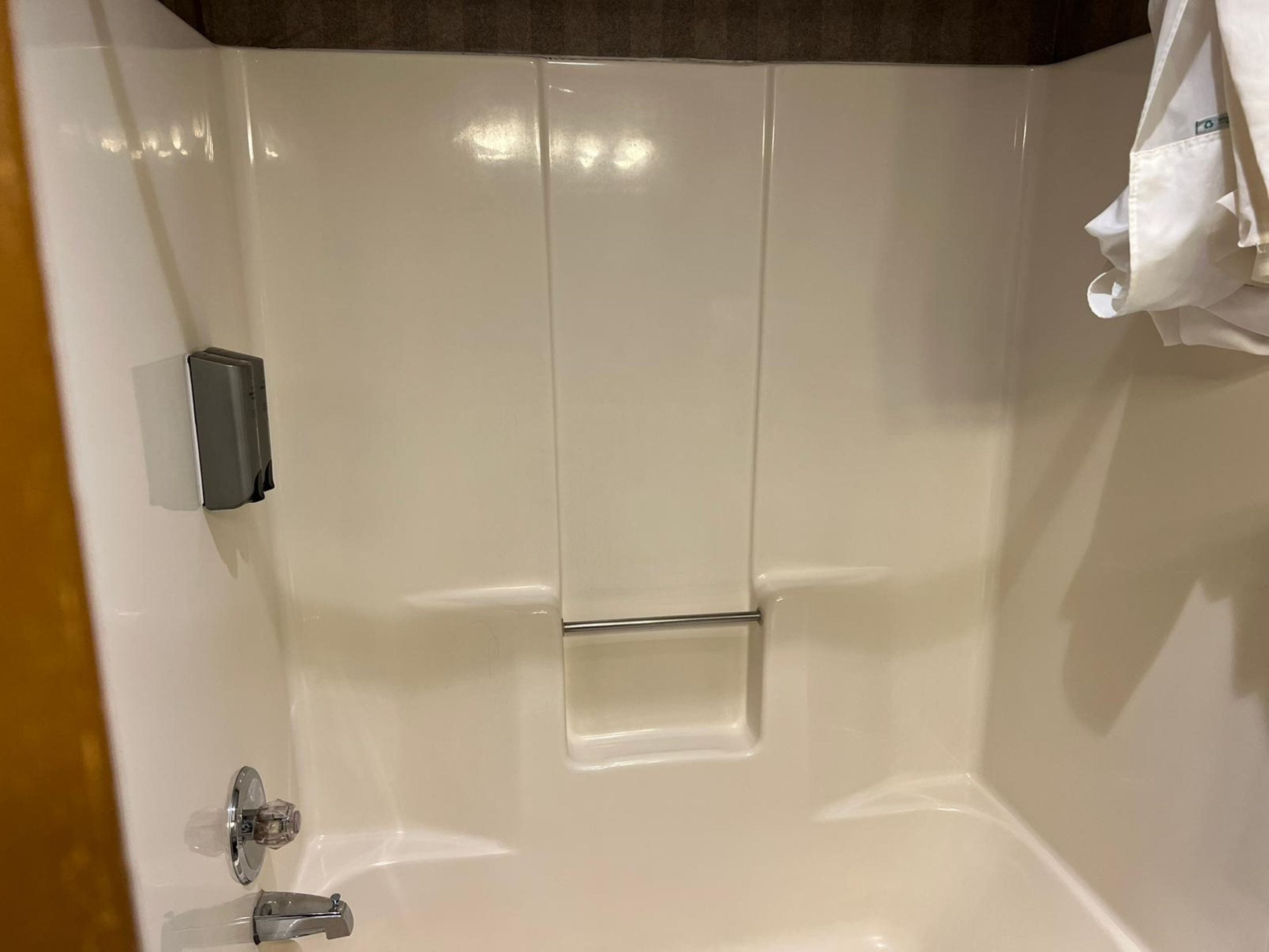 Ducha con azulejos blancos, dispensador de jabón de mano y barra para toallas.