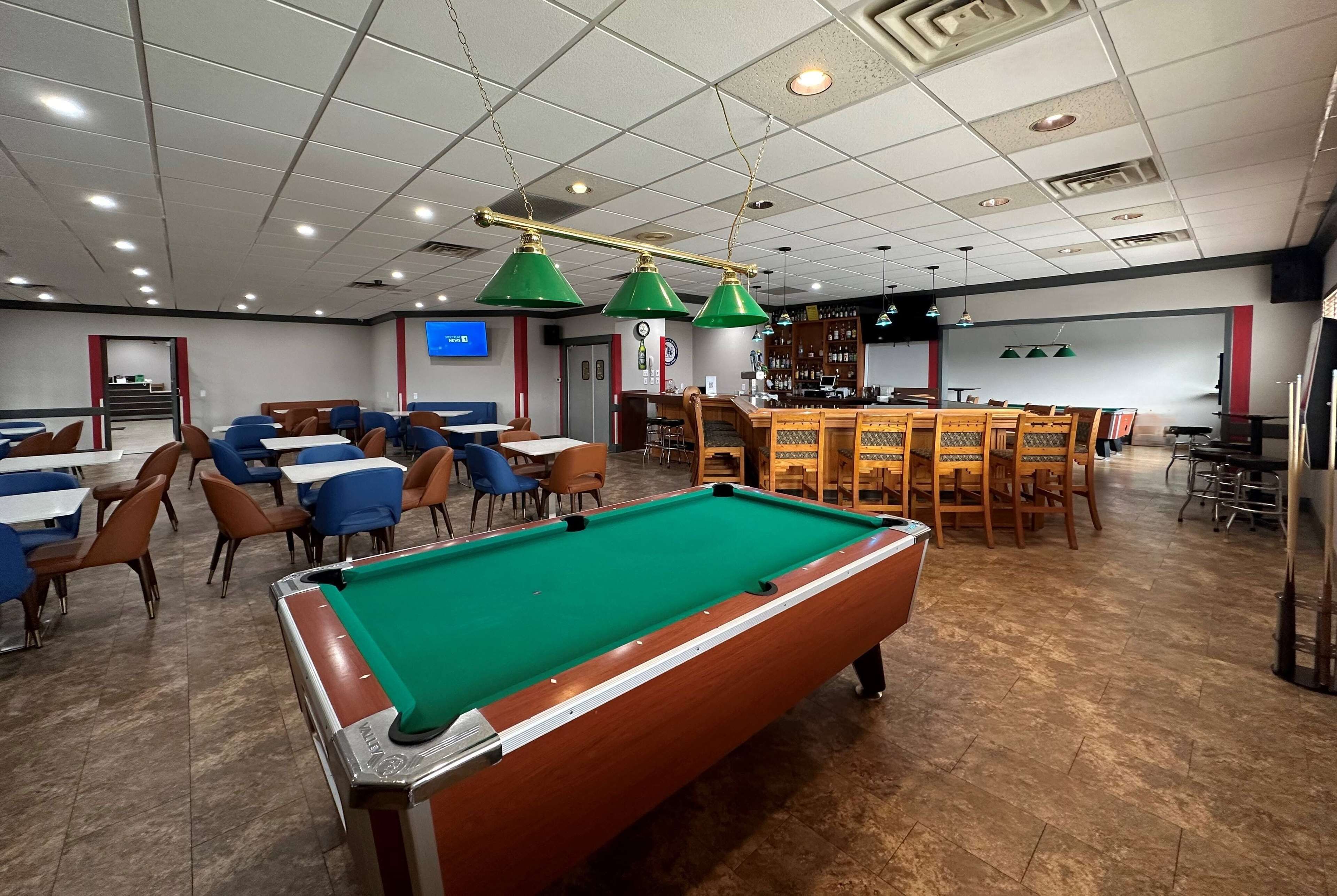 Una sala de billar con mesas y sillas, una mesa de pool y una zona de bar.