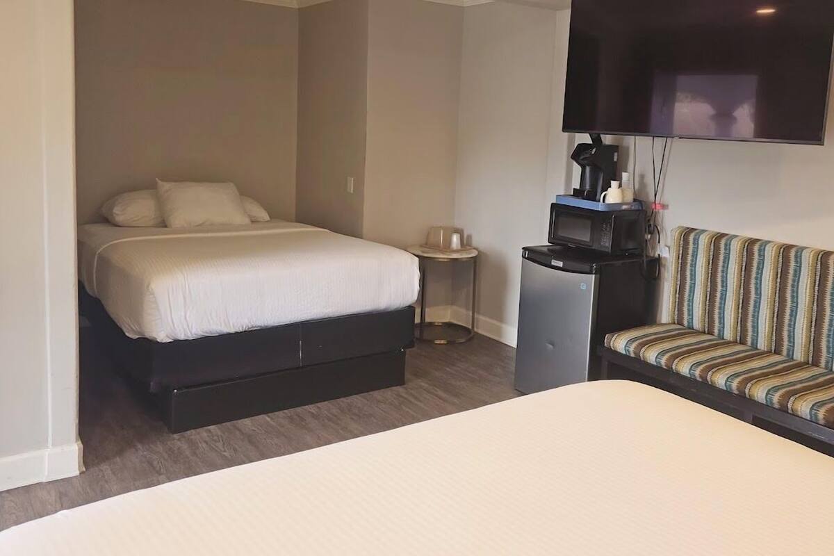 A hotel room with a bed, a small table, a microwave, a sofa, and a TV mounted on the wall.