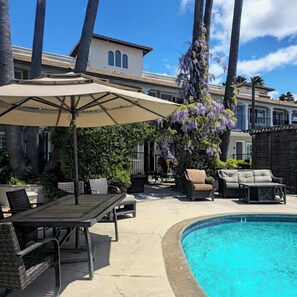 Un espace aménagé au bord de la piscine, comprenant une chaise longue, une table et un grand parasol.