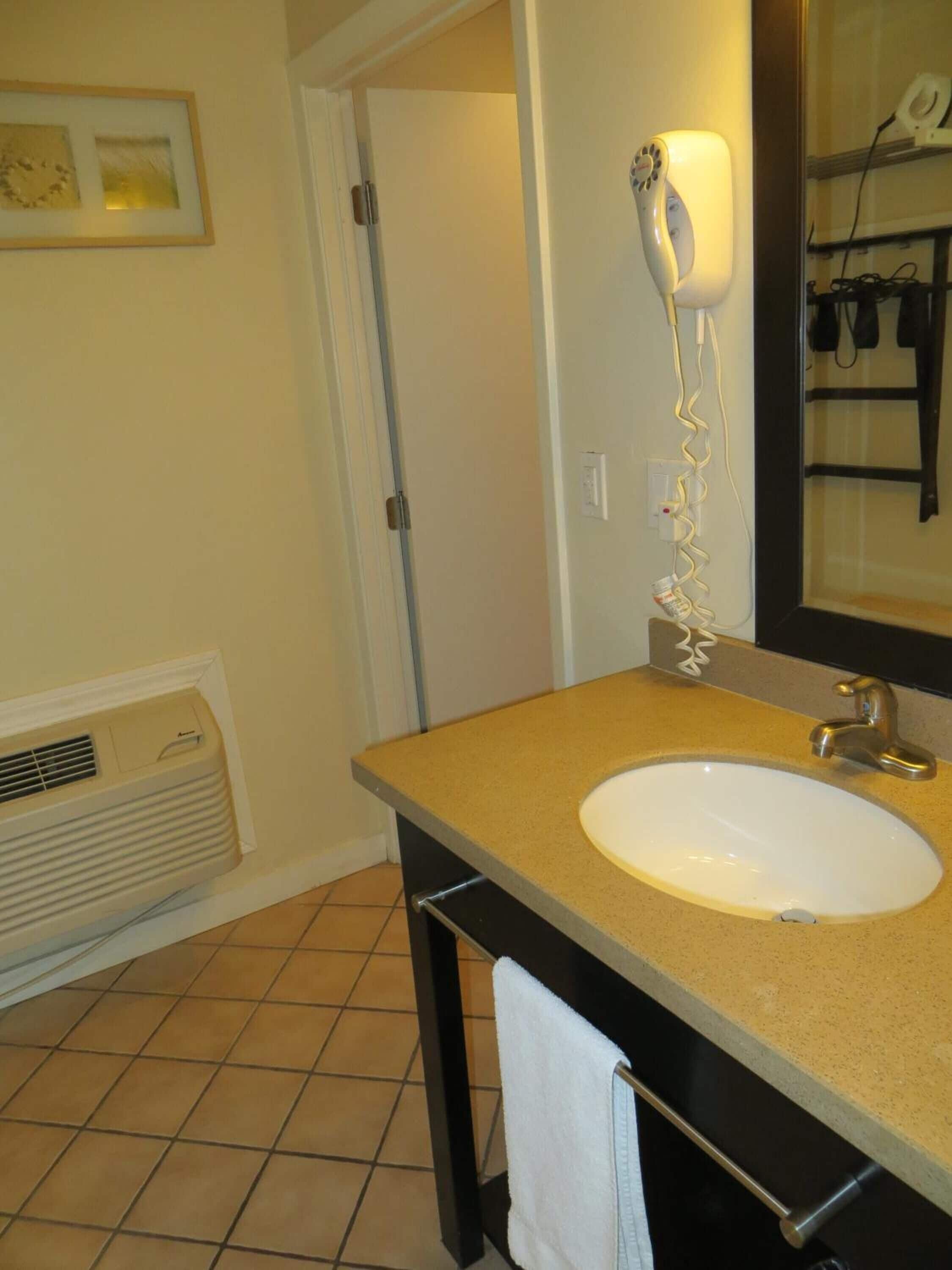 A bathroom with a beige countertop, a white sink, a towel rack, and a hairdryer on the wall.