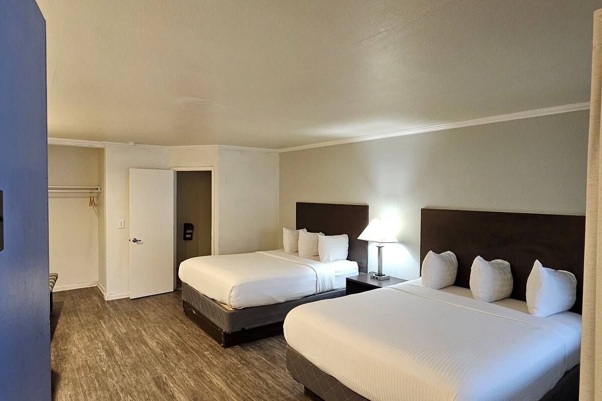 A hotel room with two beds, a wardrobe, and a door leading to a bathroom.