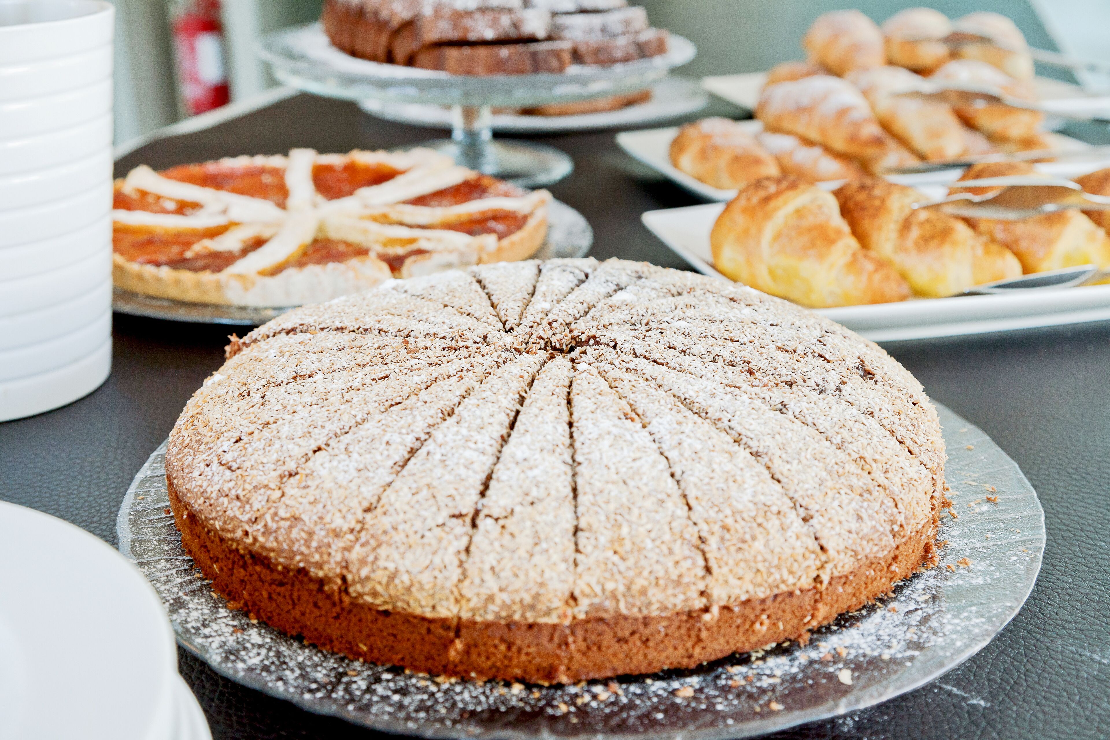 Diverse desserts op een tafel, waaronder een taart met een kruispatroon en een ronde taart bestrooid met poedersuiker.