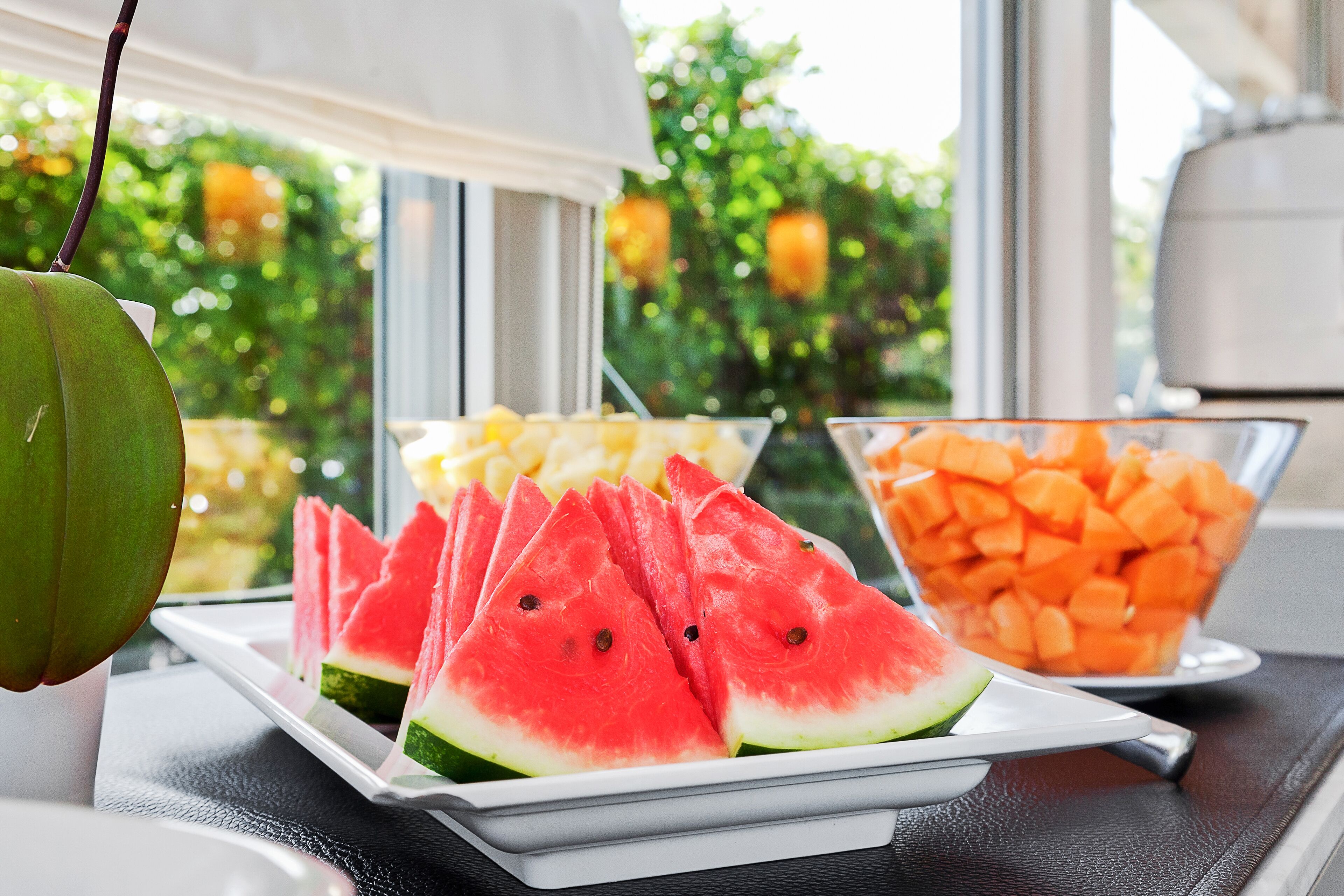 Un tavolo con una piastra di fette di anguria, una ciotola di melone cantalupo e una ciotola di carote.