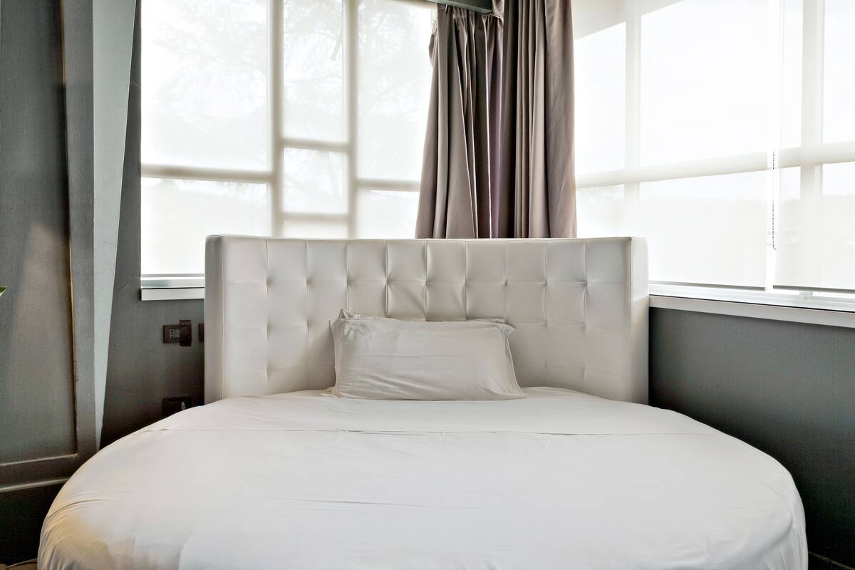 A neatly made bed with a tufted headboard in a room with a large window and curtains.